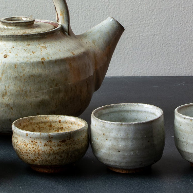 Set of ceramic teapot and four cups on a dark surface with a gray background
