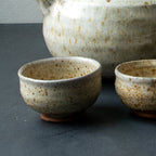 Set of ceramic teapot and four cups on a dark surface with a gray background