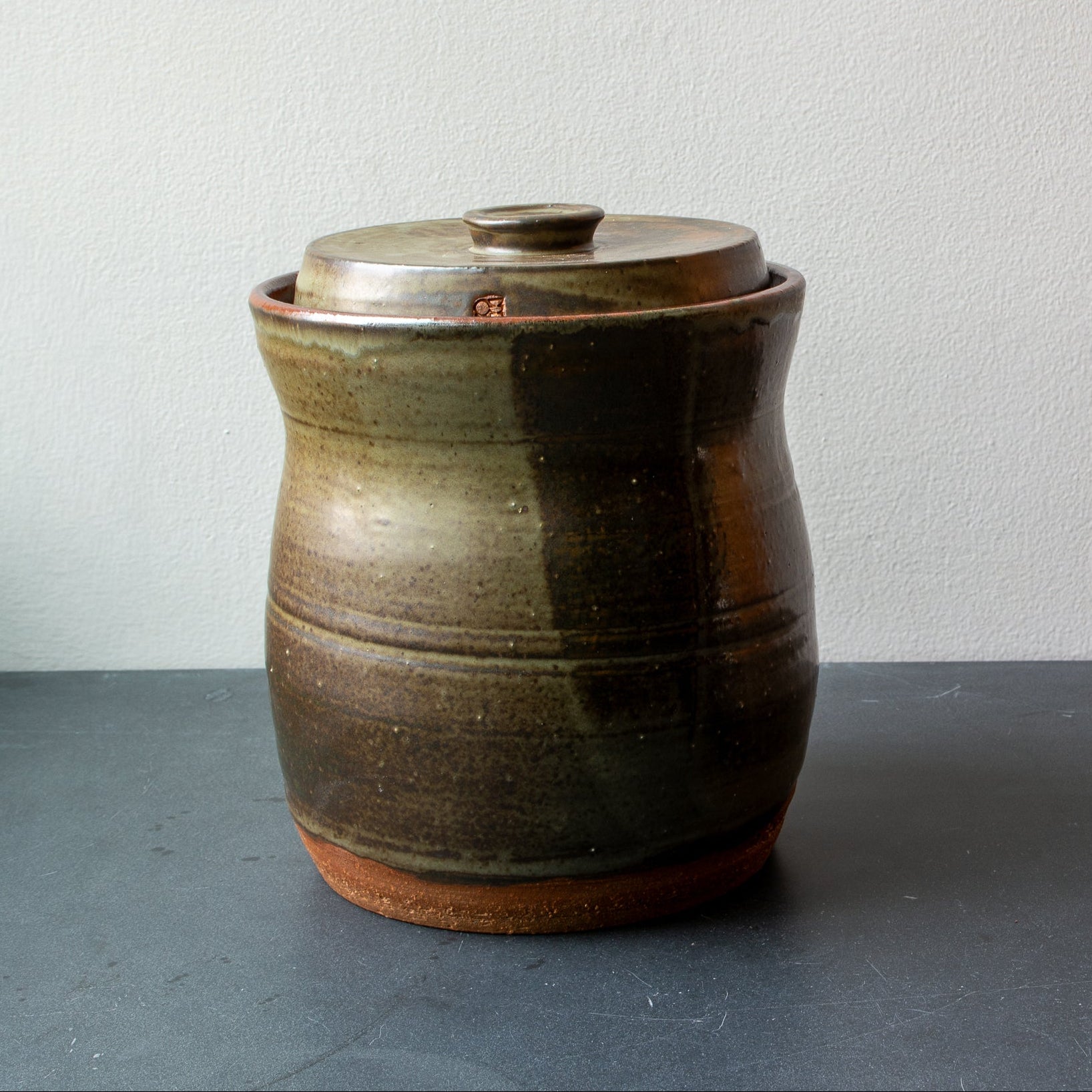 Brown ceramic jar with lid on a gray surface and light gray background